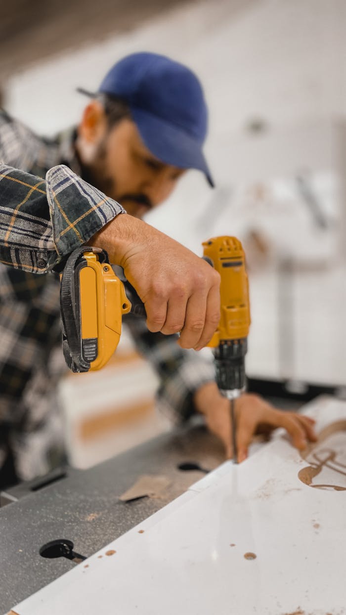 Close-up of a carpenter using a yellow drill in a workshop setting, focusing on hand.